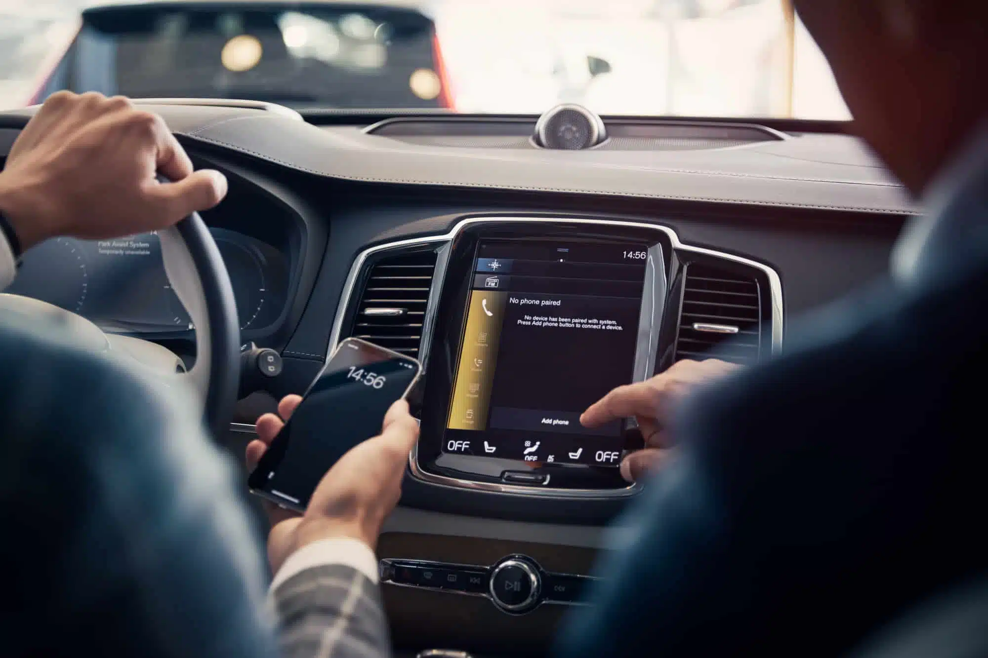 Två personer sitter i en bil. Den ena håller en mobiltelefon i handen, den andra trycker på bilens display.