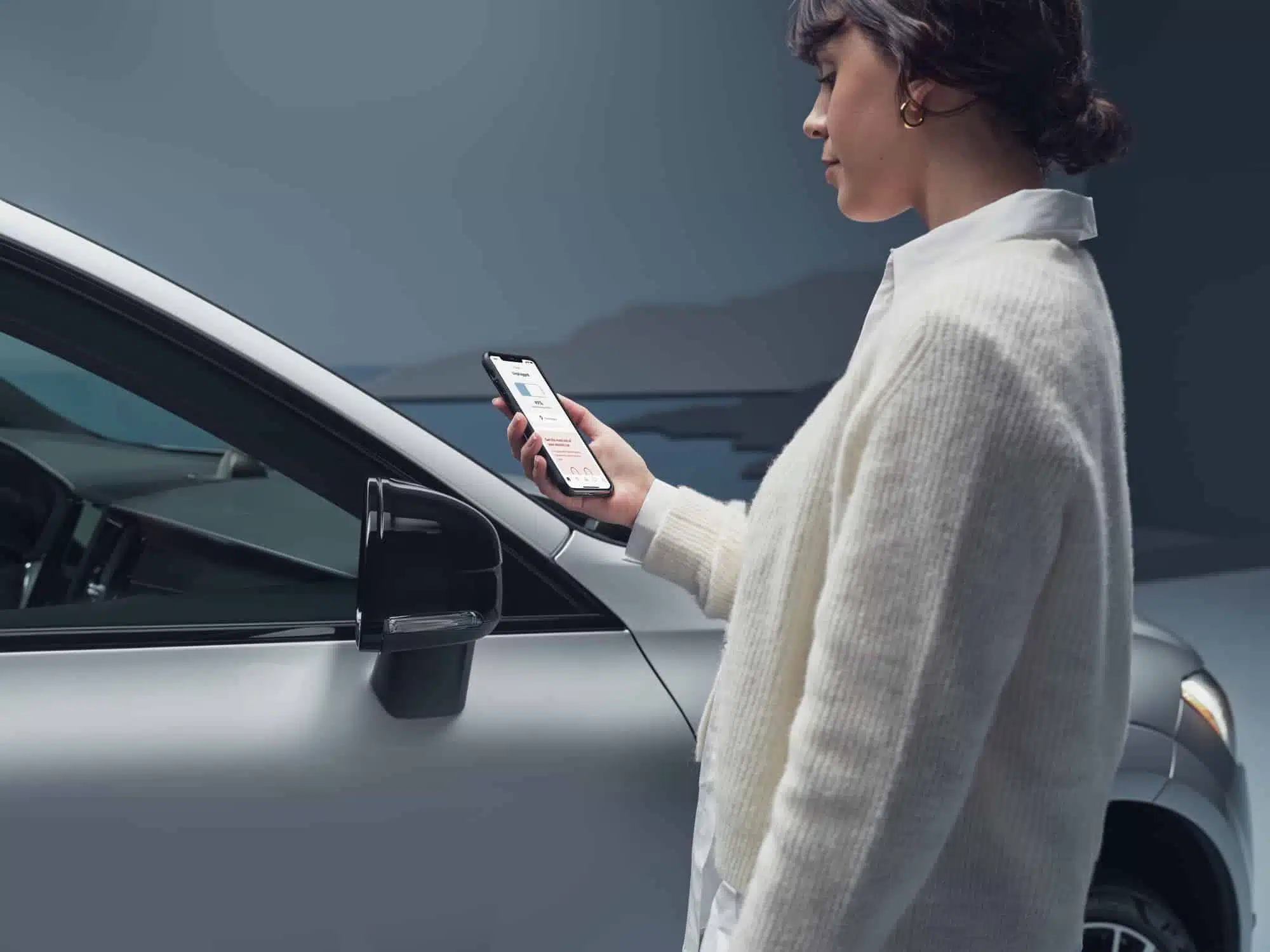 En kvinna står vid en bil och tittar i sin mobiltelefon.
