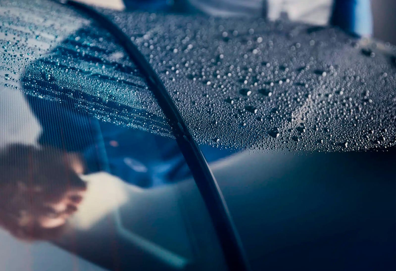 Vattendroppar speglas i en motorhuv på en blå bil.
