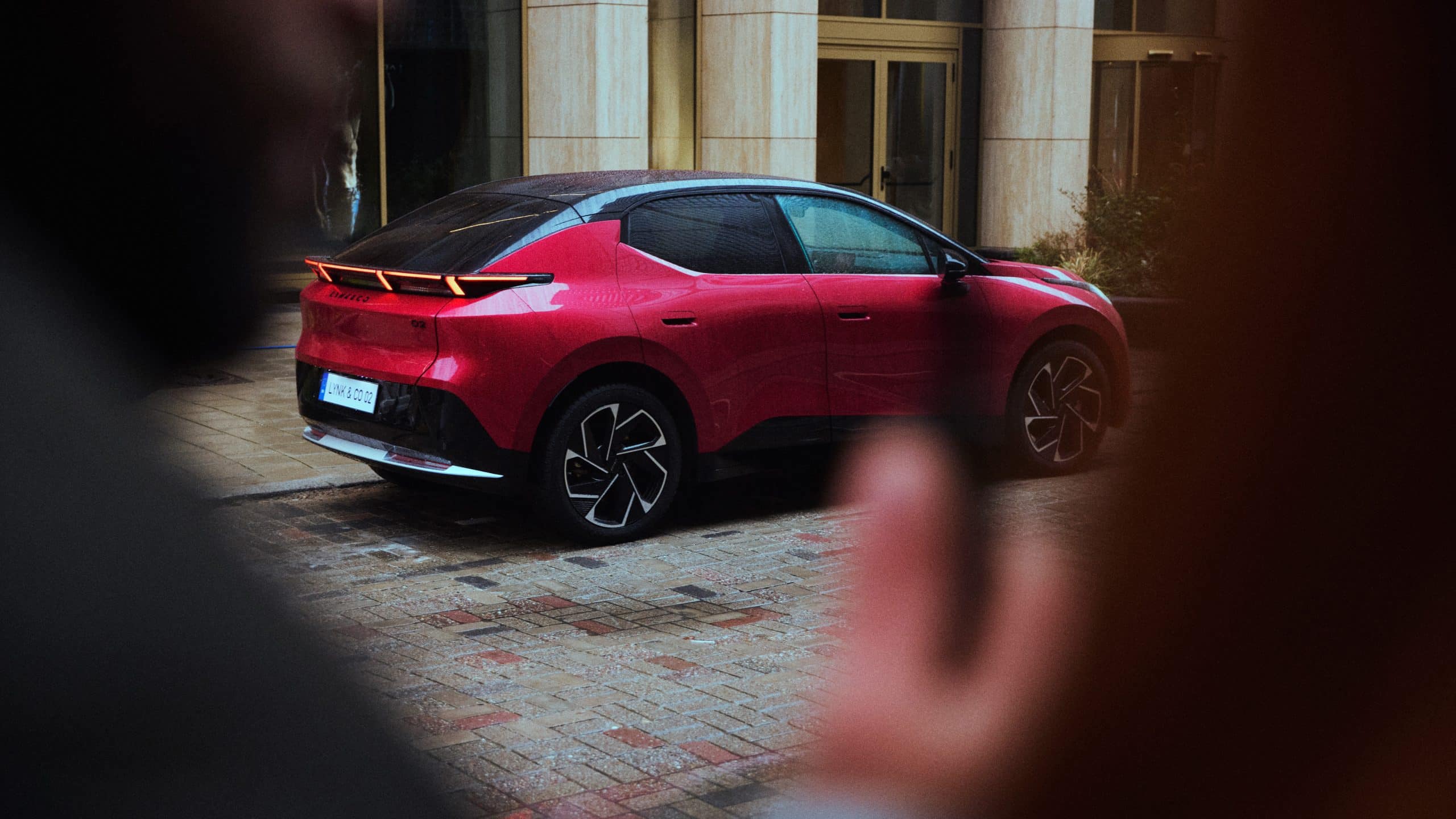 Röd bil utanför ett hotell. Bilen är en Lynk & Co 02.